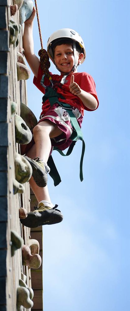 A young boy climbs the climbing wall at Camp Manitou