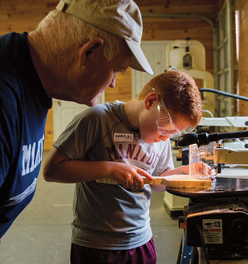 A woodworking instructor watches closely as a camper crafts a masterpiece in the carpentry shop